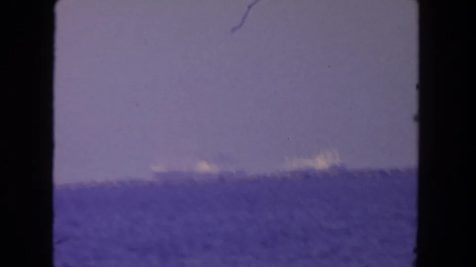 Soft 1962 home-movie frame of a low maritime horizon, with blue water and faint ship shapes in the distance.