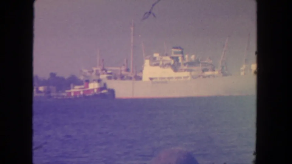 1962 San Diego 8mm frame showing a large white cargo vessel with a smaller red-and-white boat nearby on coastal water.