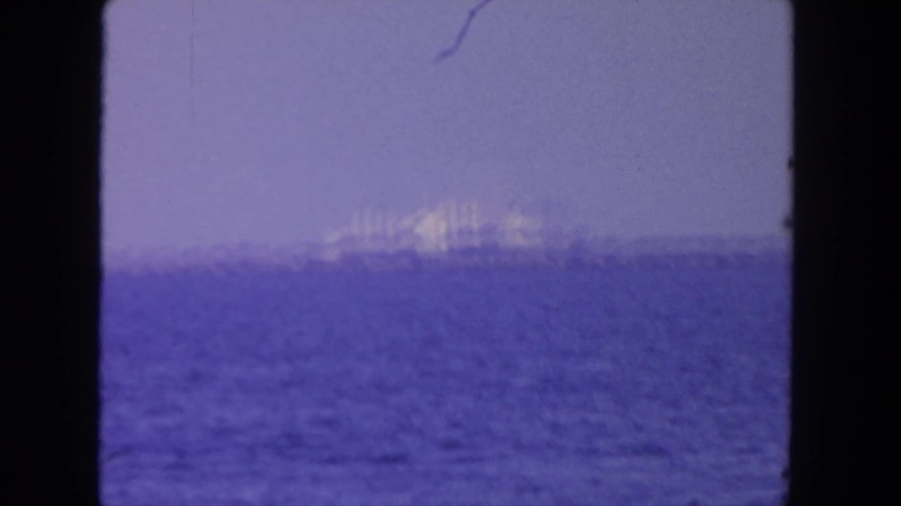 Soft 8mm view of a large ship offshore in the supplied San Diego setting, seen through haze over purple-blue water.