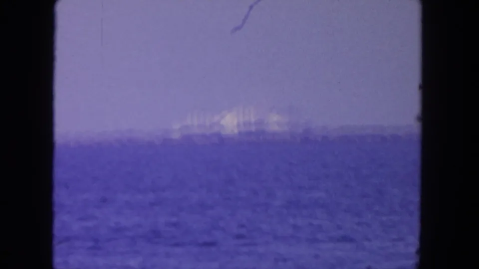 Soft 8mm view of a large ship offshore in the supplied San Diego setting, seen through haze over purple-blue water.