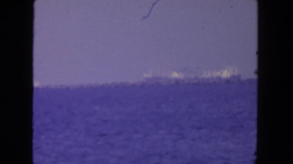 Final 8mm frame showing the large ship low and distant on the San Diego ocean horizon, softened by motion, haze, and faded color.