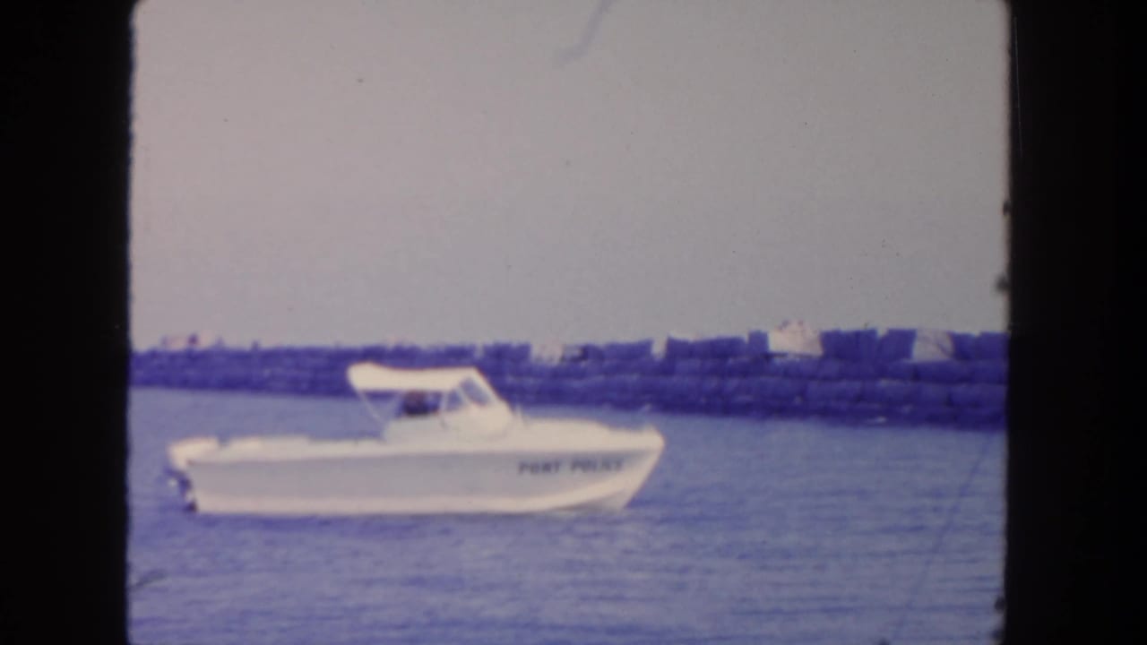 White Port Police boat moving on blue water near a low breakwater.