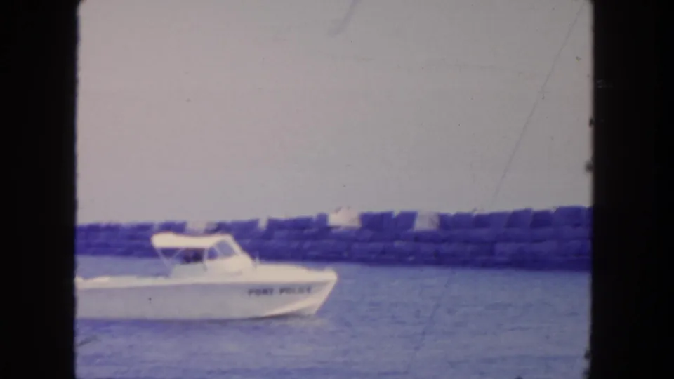1962 San Diego harbor view with the Port Police boat partly across frame, backed by a low breakwater and distant waterfront shapes.