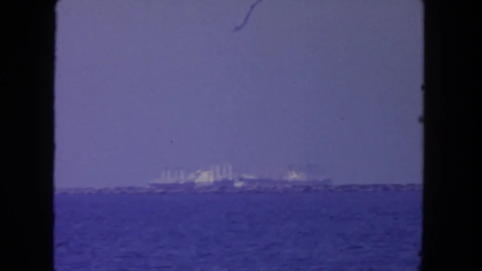 1962 San Diego 8mm frame looking over blue harbor water toward distant ships or waterfront industrial structures on the horizon.