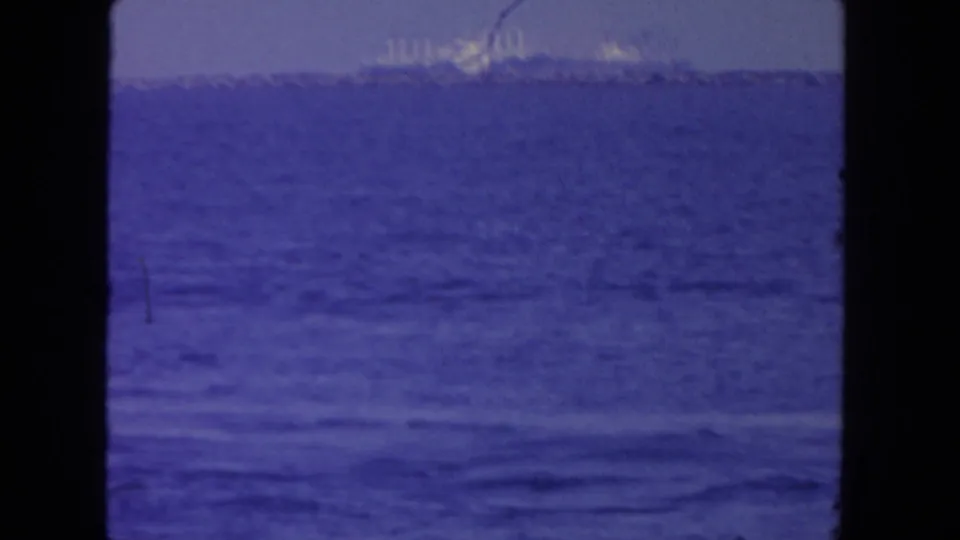 1962 San Diego harbor frame showing rippled blue water and distant bright ships or industrial structures through soft 8mm exposure.