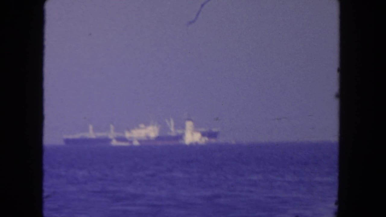 1962 San Diego harbor view with a distant large vessel beyond calm blue water and dark 8mm frame edges.