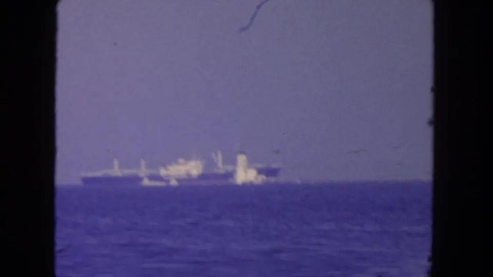 1962 San Diego harbor view with a distant large vessel beyond calm blue water and dark 8mm frame edges.