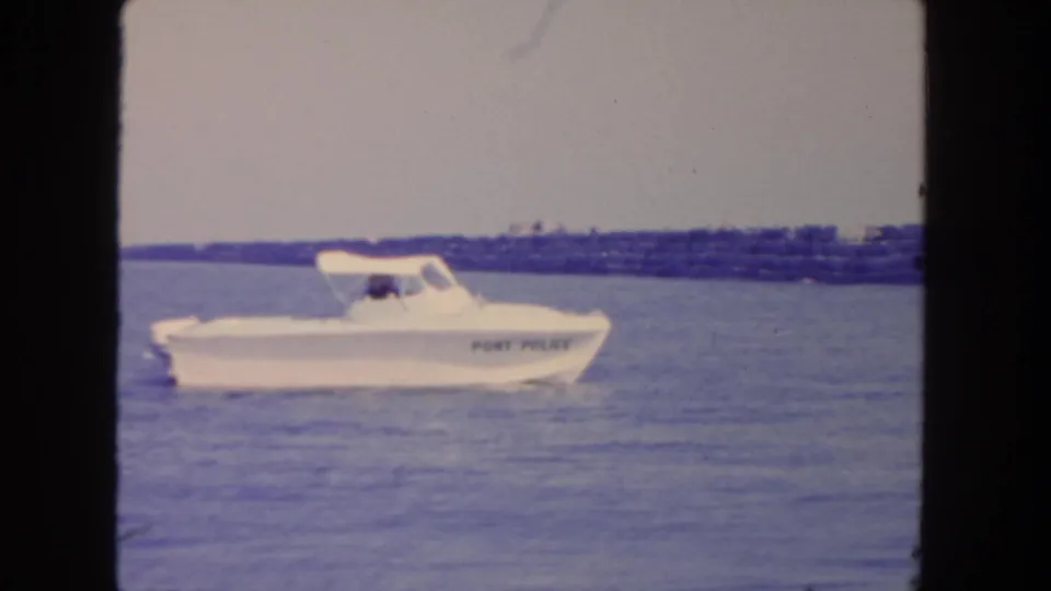 White port police boat moves across San Diego harbor water near a low breakwater in 1962 home-movie footage.