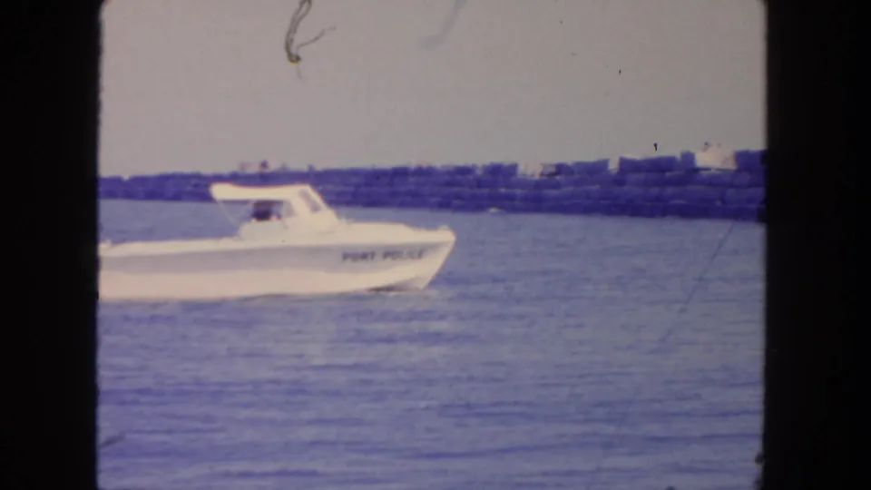 A white port police boat passes close to frame left with a San Diego harbor breakwater in the background.