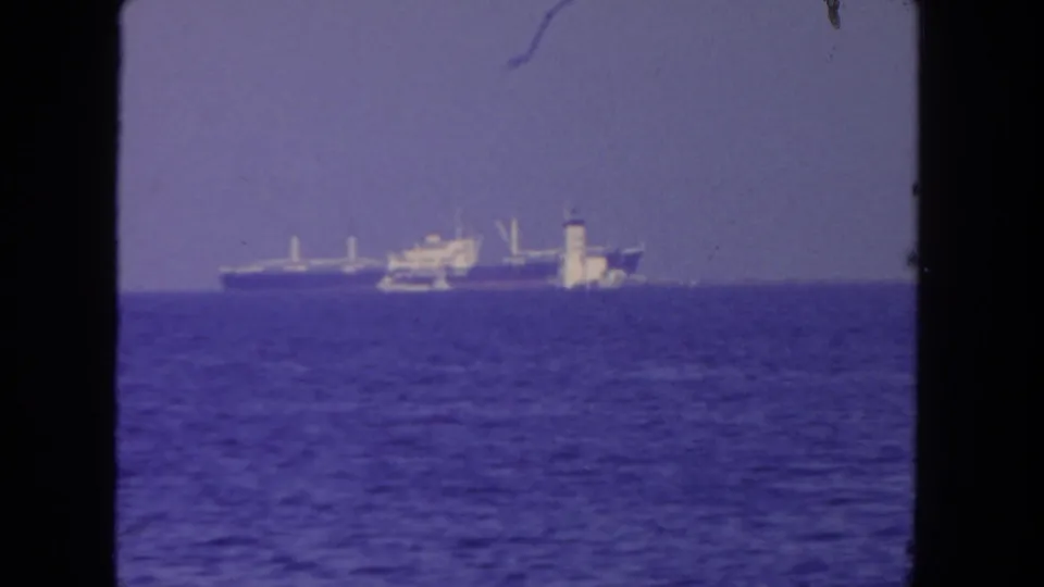 1962 San Diego home-movie frame with a distant cargo ship and smaller vessel on the horizon, bordered by dark 8mm film edges.