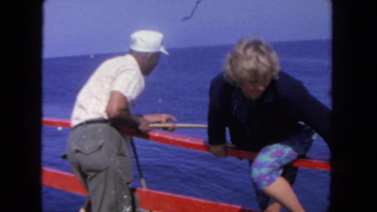 The woman leans across the red rail during boarding as the man stands close by, with deep blue ocean visible in the San Diego setting.