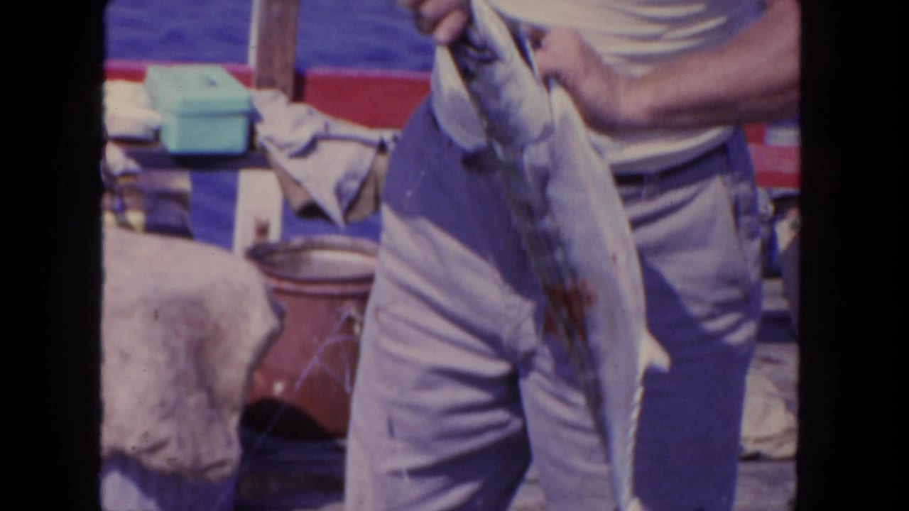 Man in a white shirt holds a large fish beside a red boat railing.