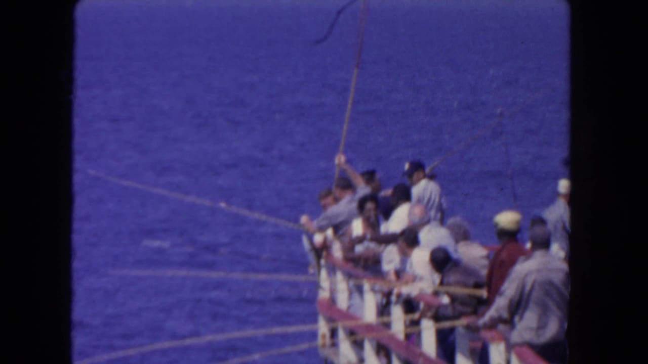 Men fish from the side of a boat on open blue water.