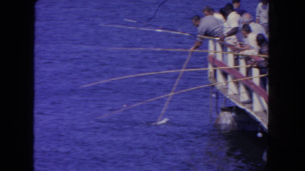 Several men fish from a San Diego pier in 1962, leaning over railings with long rods above blue water.