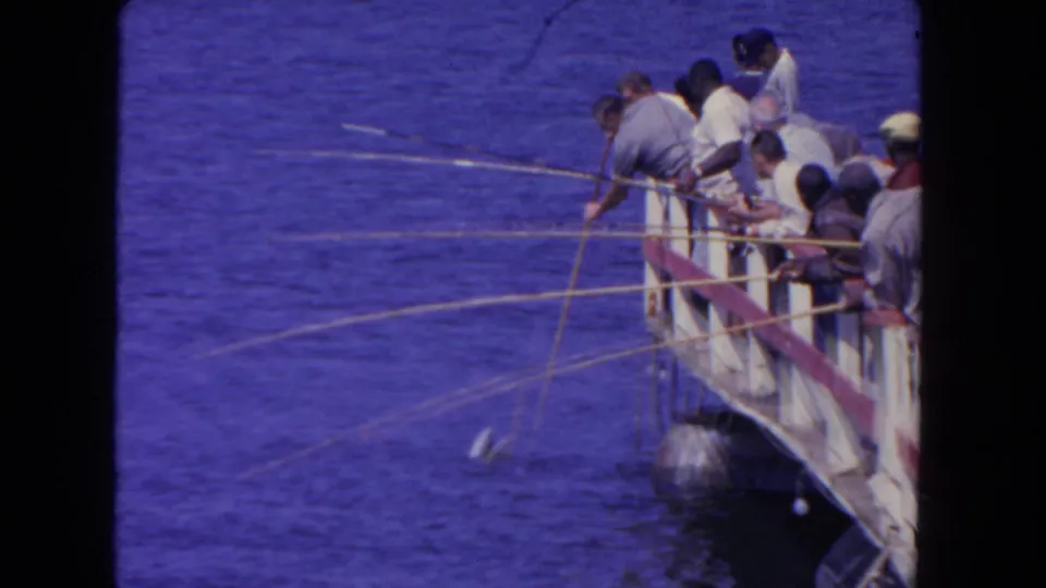 A closer 8mm view shows men gathered along the San Diego pier railing with rods angled toward the water.