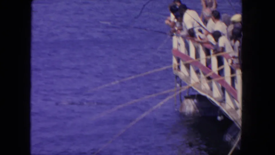 Home-movie frame of anglers clustered at a pier railing in San Diego, with fishing lines stretching across the water.