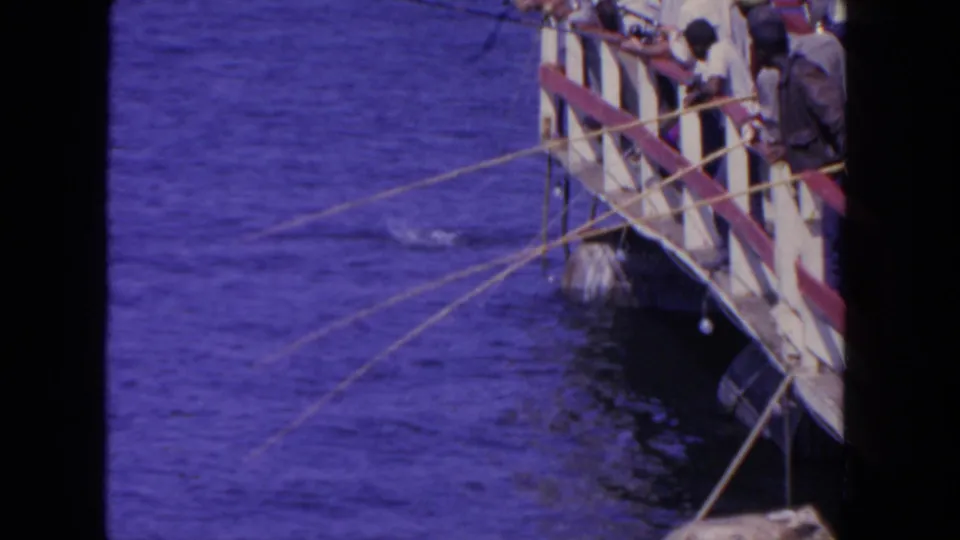 1962 San Diego pier scene with people at the railing, fishing lines crossing the frame, and blue water below.