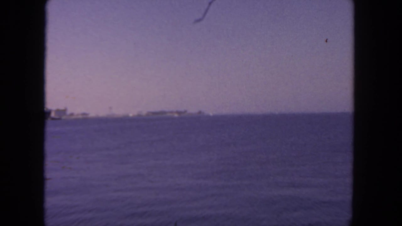 1962 San Diego harbor view across open water with distant vessels under a faded purple sky.