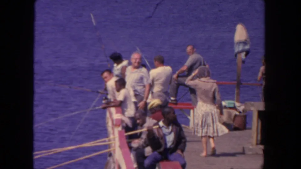 Adults on a San Diego pier or dock in 1962 stand and sit near fishing rods beside the harbor water.