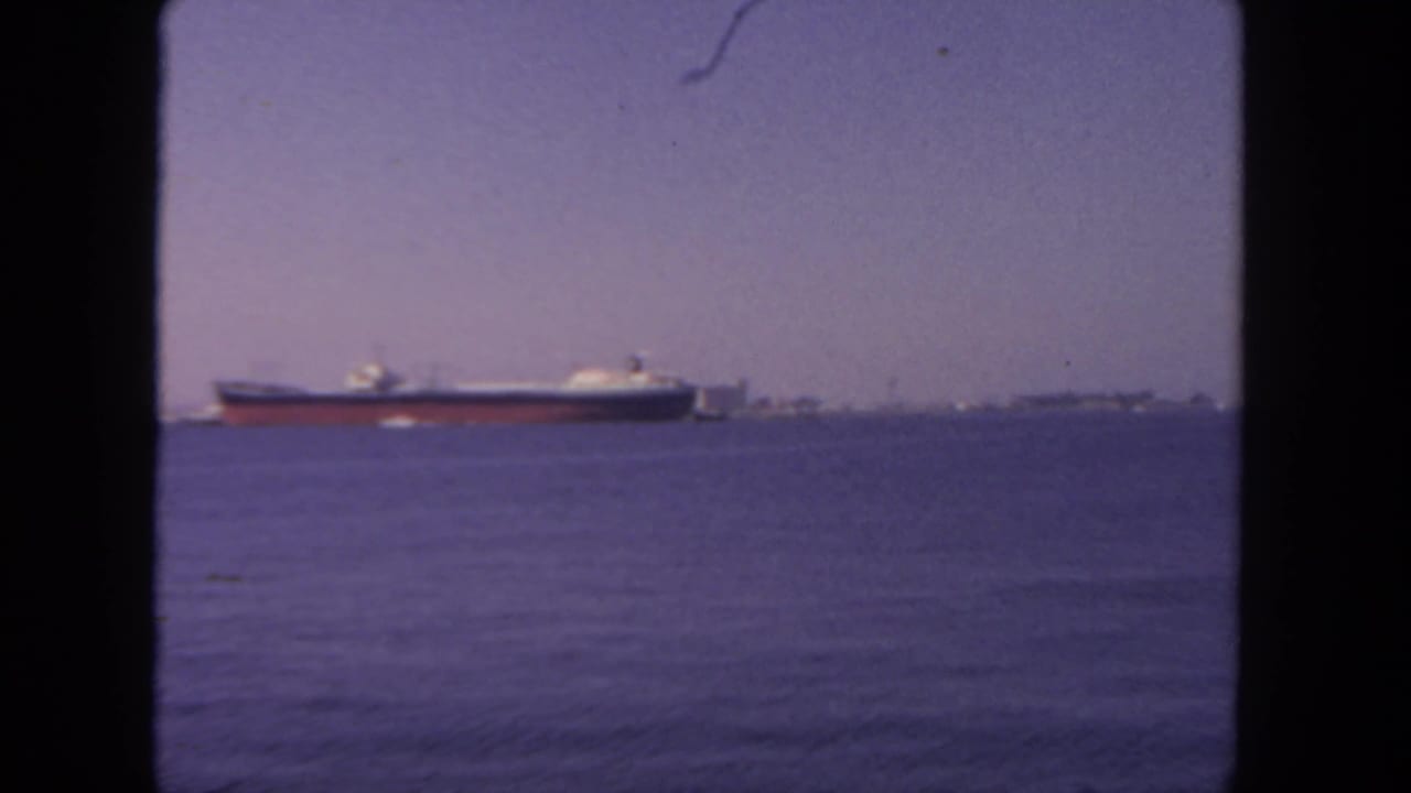 Distant freight ship on open water with a hazy shoreline and dark 8mm frame borders.