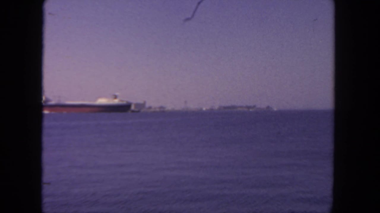 Freighter partly left of center on calm water with distant shoreline beneath a hazy sky.