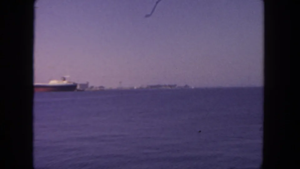 Handheld 8mm frame likely near San Diego, with the ship moving out of view and the distant urban shoreline becoming more prominent.