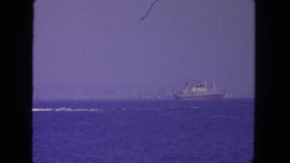 1962 8mm view off San Diego showing a distant ship on open water with a faint coastline under a hazy purple-blue sky.