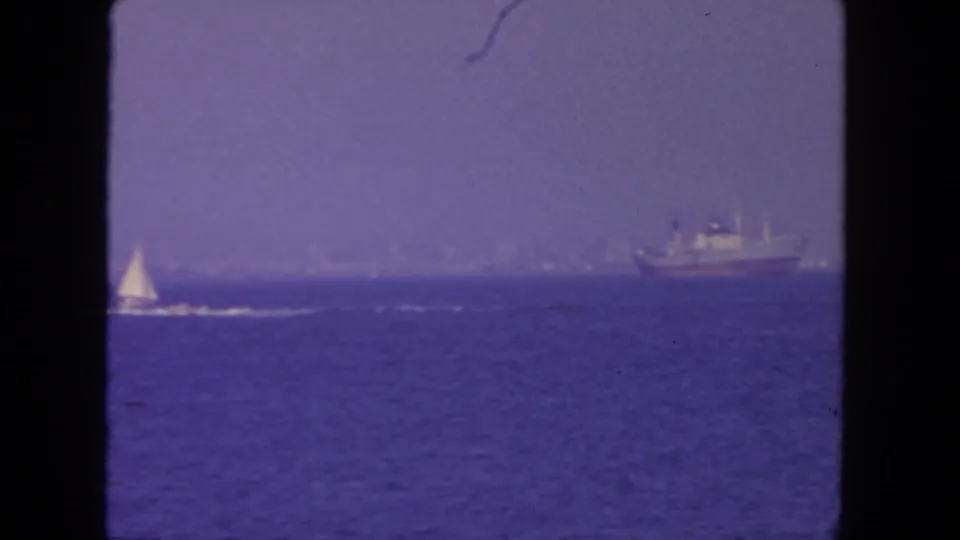 1962 San Diego coastal footage shows a small sailboat in the foreground distance and a larger ship farther along the horizon.