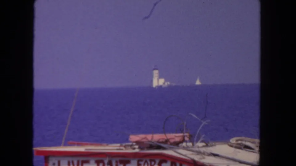 1962 San Diego 8mm frame with a boat deck at the bottom, a distant shoreline structure, and small sailboats on the ocean horizon.