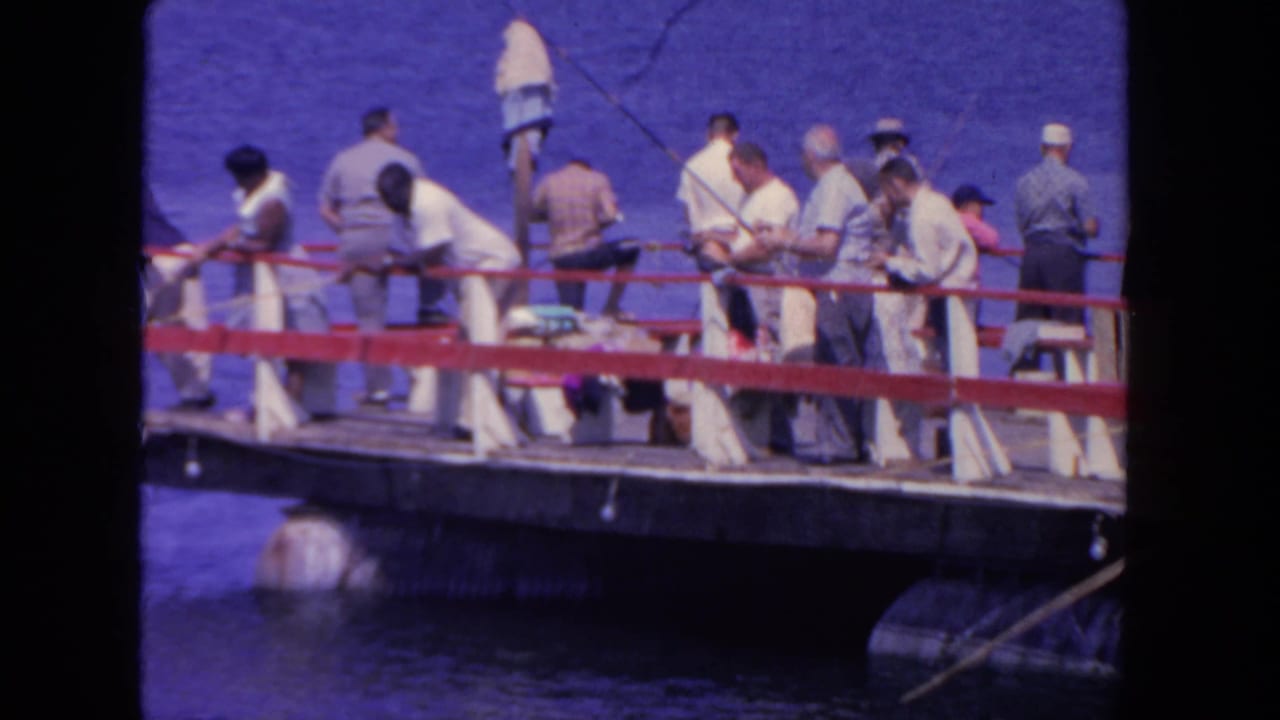 Men fishing from a red-railed wooden pier over blue harbor water.