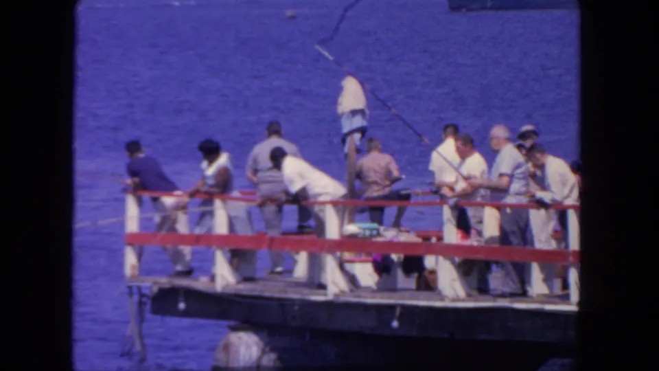 A 1962 San Diego harbor view shows men clustered along a red railing while fishing from a wooden pier.