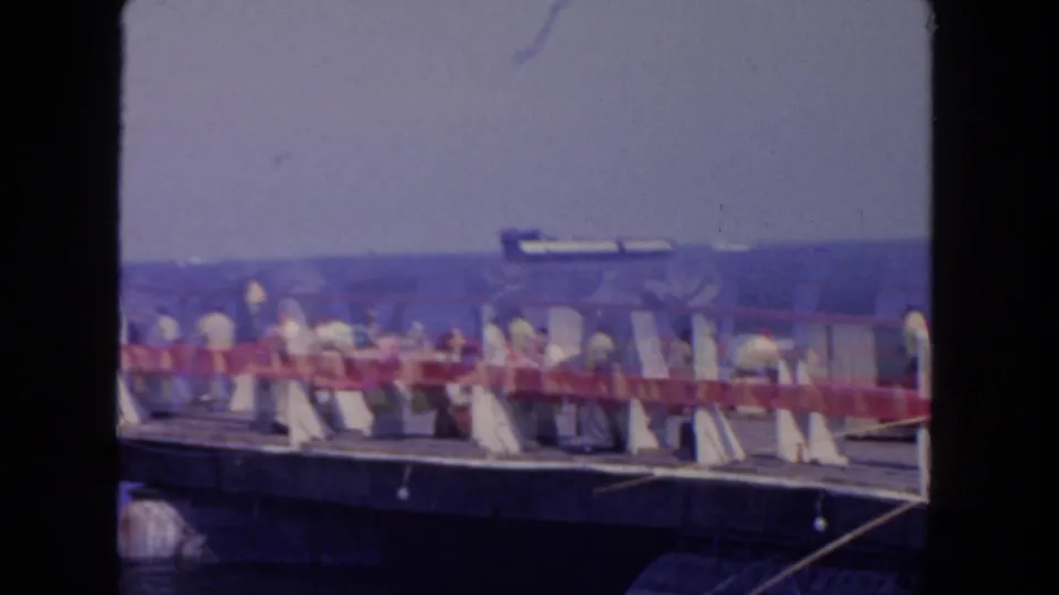 Soft 8mm frame from the San Diego pier, with figures near the railing, blue water, and a distant ship partly visible through film blur.