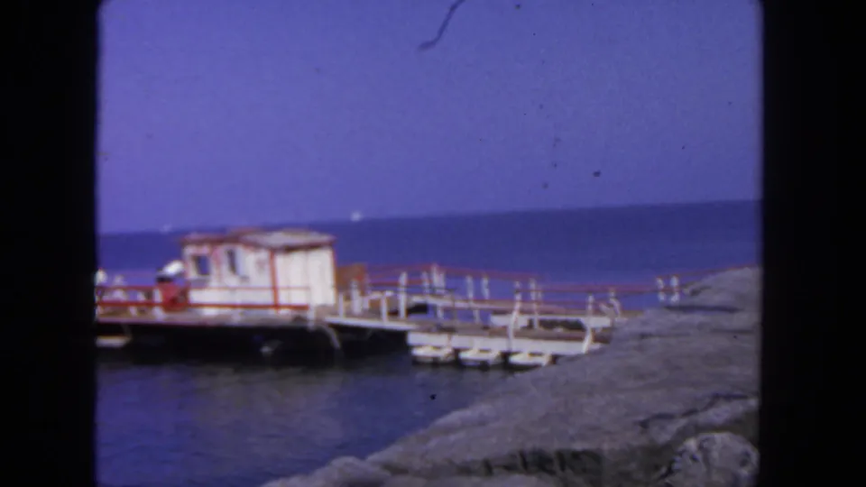 1962 San Diego 8mm frame showing the red-trimmed white pier shack, railing, calm water, and rocky shoreline.