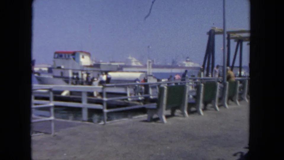 Passengers move along the San Diego dock near the ferry, with railings, pier structures, and harbor water behind them.