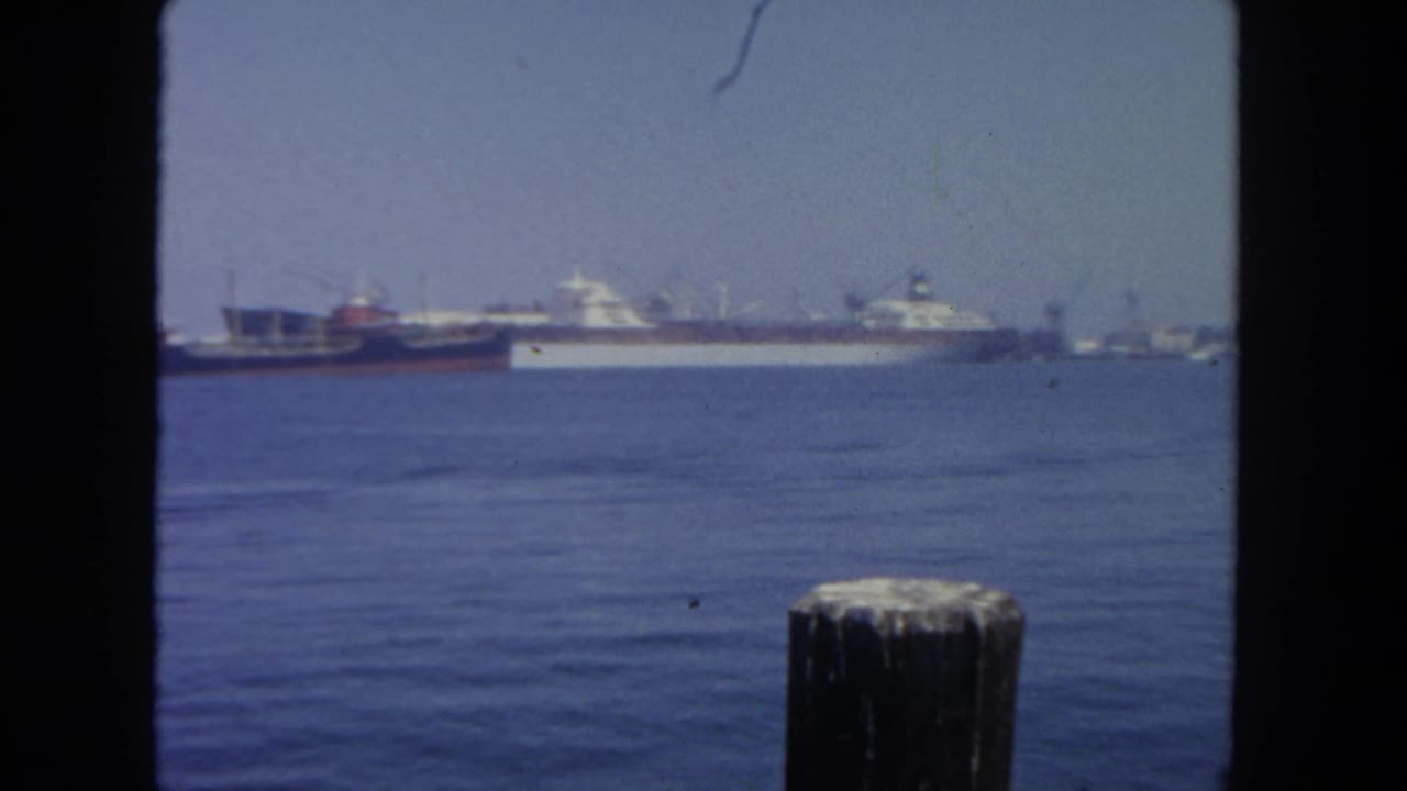 Harbor water with distant cargo ships seen through dark film-frame edges.
