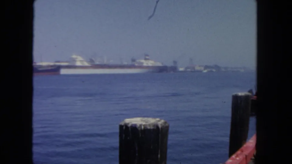 San Diego harbor in 1962, with cargo vessels on the horizon, calm water, a foreground dock post, and visible 8mm gate edges.