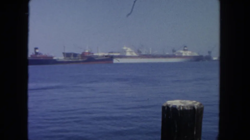 San Diego harbor scene from 1962 with anchored ships in the distance and a dark pier piling against calm blue water.
