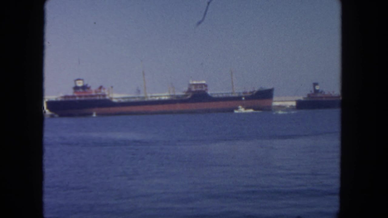 1962 San Diego harbor view with cargo vessels, tugboats, blue water, and a dark window-like frame around the scene.