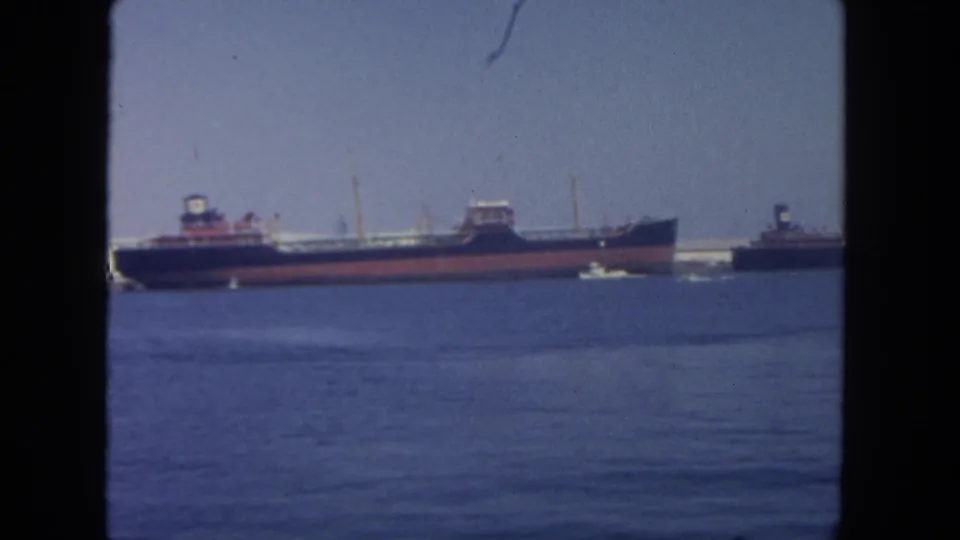 1962 San Diego harbor view with cargo vessels, tugboats, blue water, and a dark window-like frame around the scene.