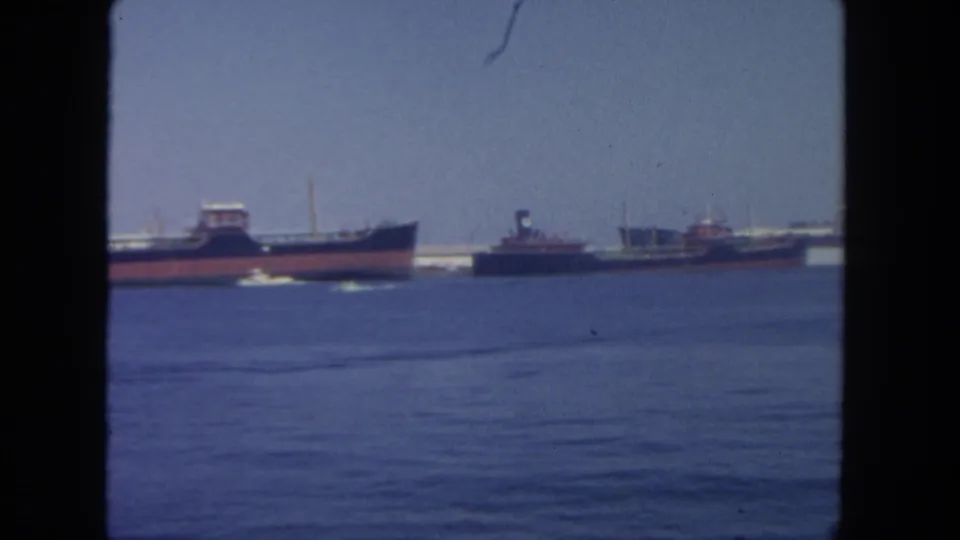 1962 San Diego harbor frame with tugboats, cargo vessels, calm blue water, a pale sky, and dark 8mm frame borders.