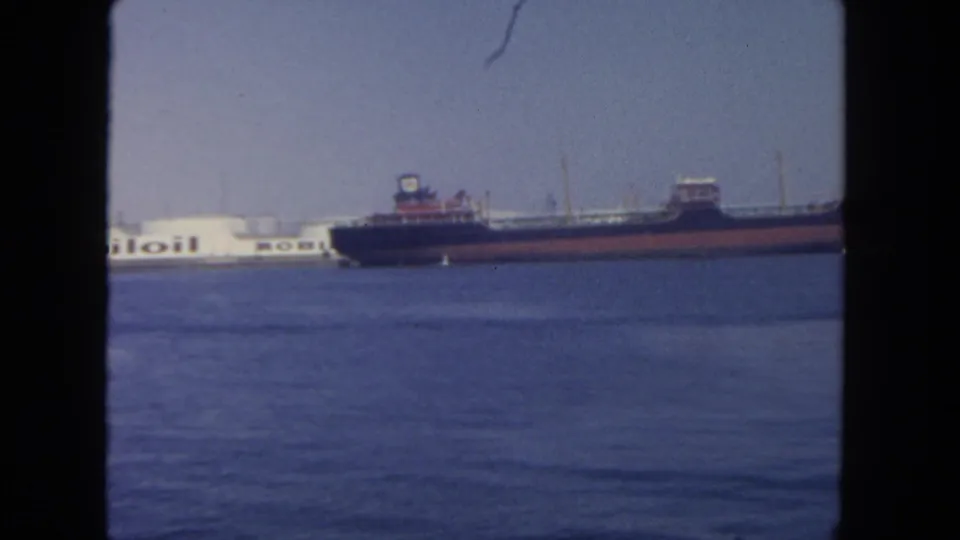 Distant 1962 San Diego harbor frame showing a cargo ship beside the visible Mobil tanker lettering, with open water in the foreground.