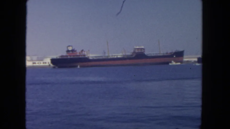 1962 San Diego harbor footage frame with the cargo ship more centered, a Mobil tanker behind it, and small white boats near the right edge.