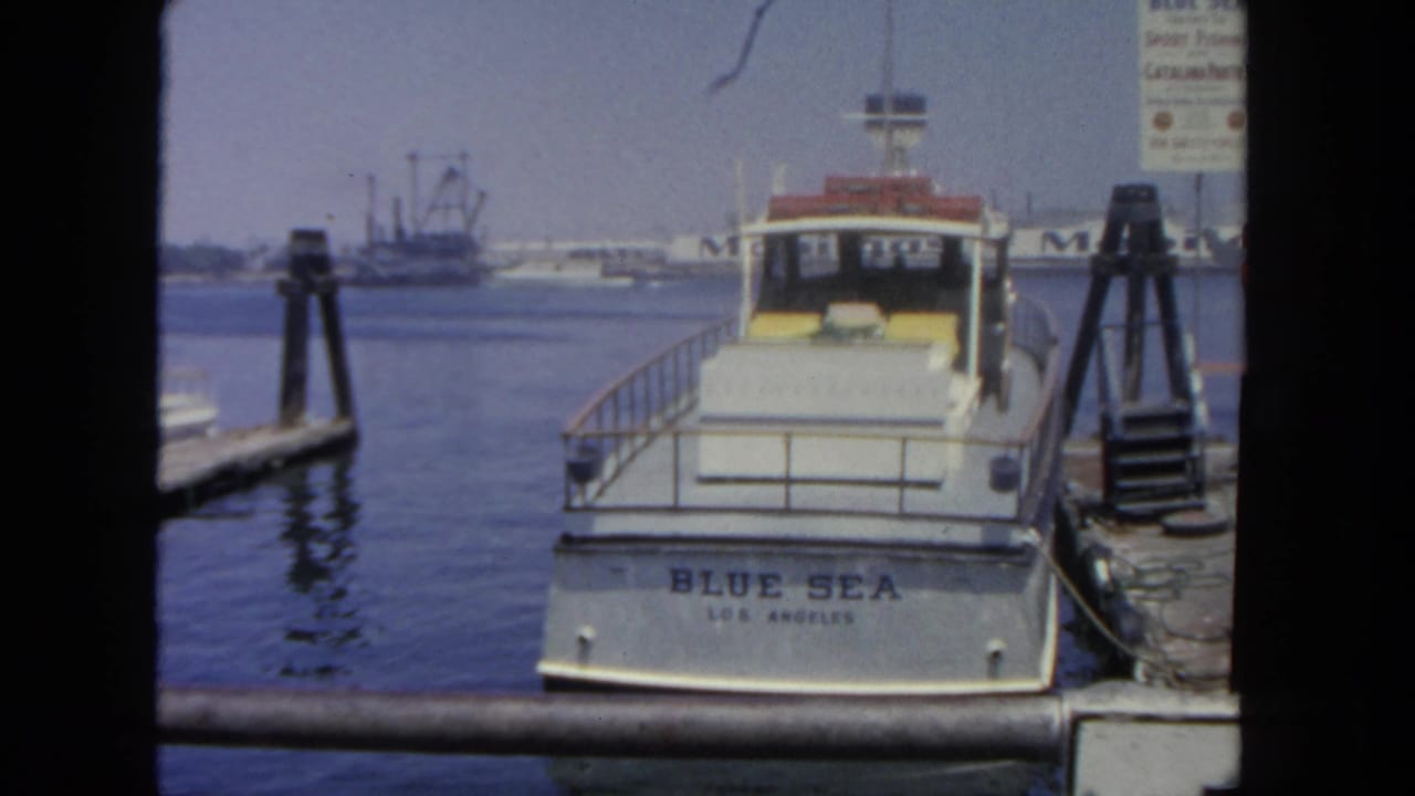 Blue Sea boat seen from behind at a dock, framed by dark 8mm film borders.