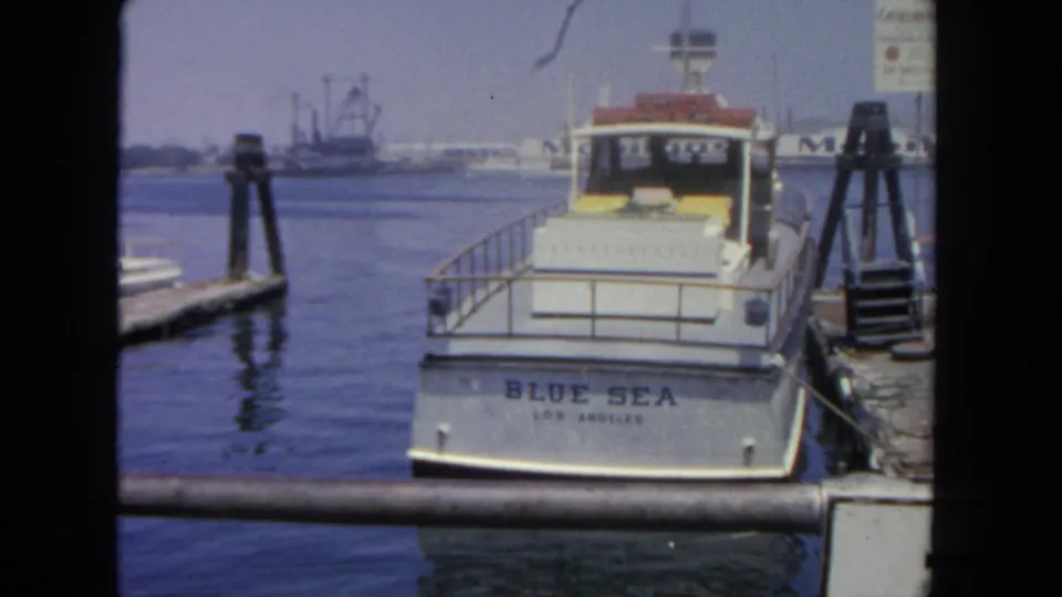 1962 San Diego marina shot of the stern of a white boat labeled BLUE SEA LOS ANGELES with harbor structures in the distance.