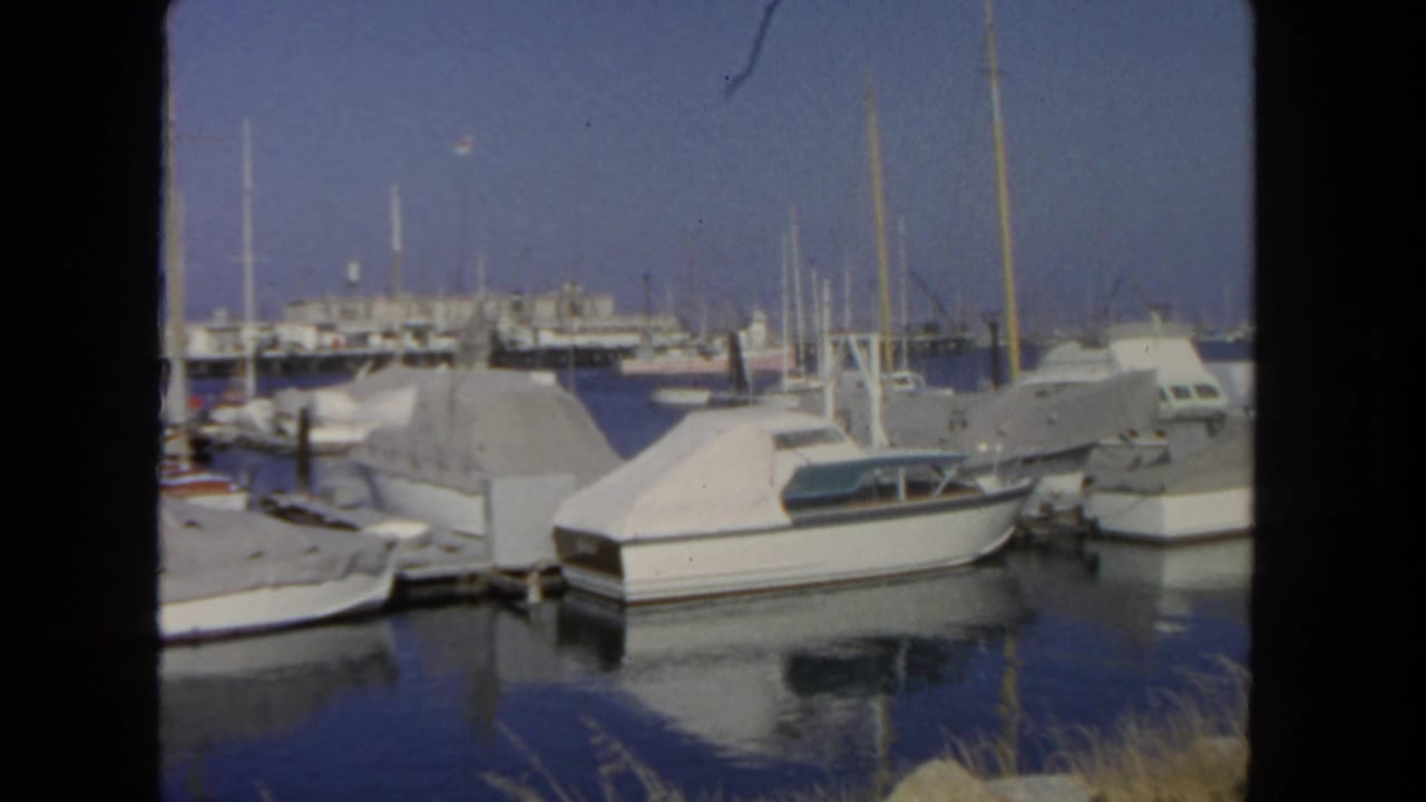1962 San Diego harbor view with covered cabin boats, docks, masts, and reflections on calm water.