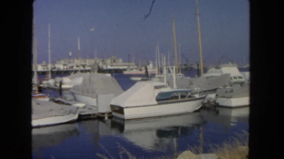 1962 San Diego harbor view with covered cabin boats, docks, masts, and reflections on calm water.