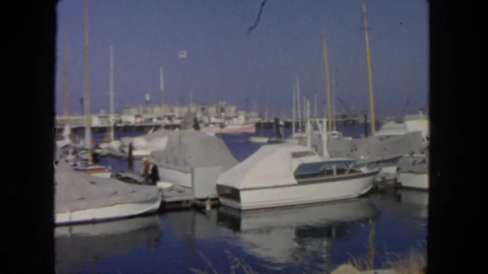 1962 San Diego marina scene showing white boats under covers, dock pilings, reflections, and a person near the dock.