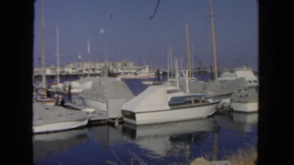 1962 San Diego waterfront marina with moored covered boats, sailboat masts, dock structures, and calm blue water.