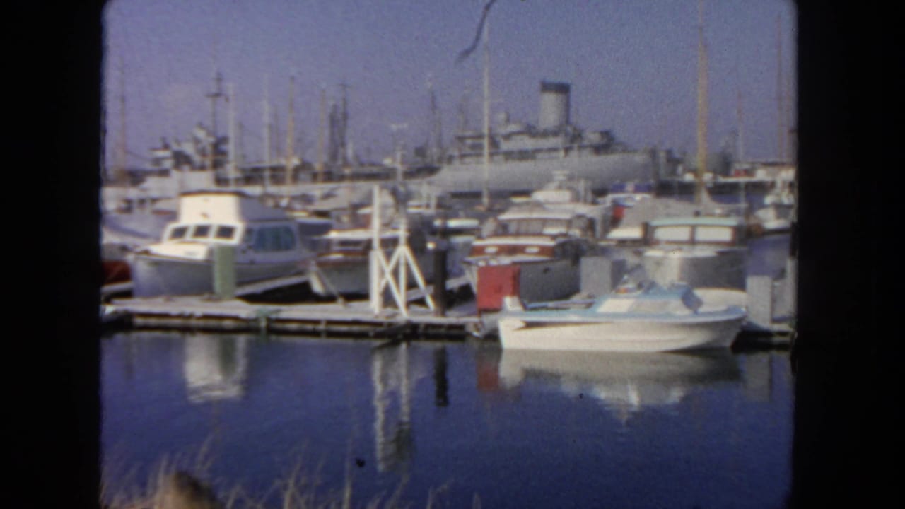 1962 San Diego marina view with small motorboats, masts, calm water, and a large passenger liner beyond the docks.