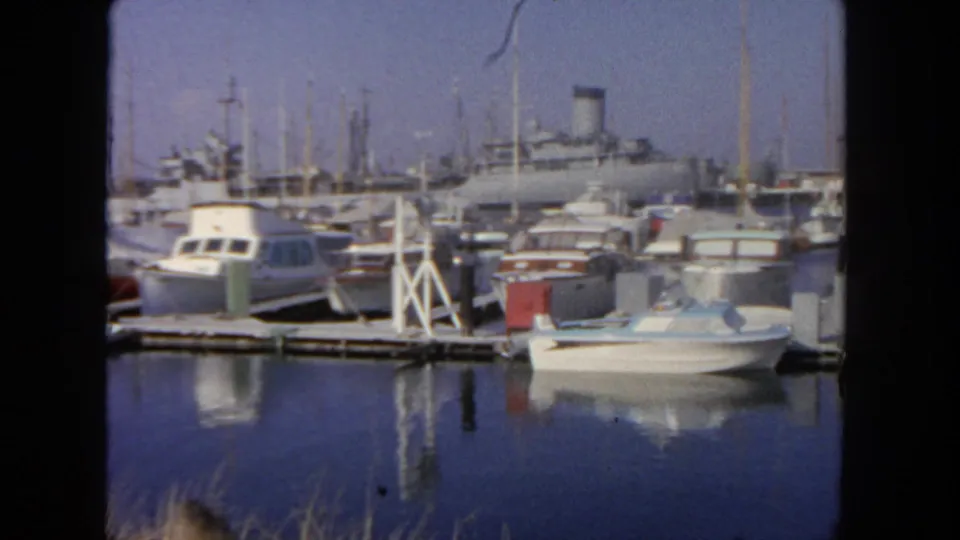 1962 San Diego marina view with small motorboats, masts, calm water, and a large passenger liner beyond the docks.